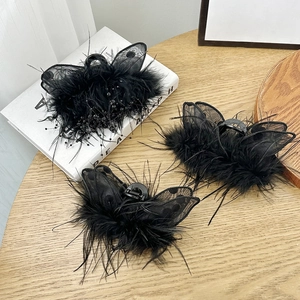 Three elegant black ostrich feather hair claws with mesh and beads on a wooden table