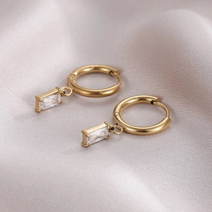 Minimalist gold hoop earrings with rectangular clear zircon pendants on silk fabric