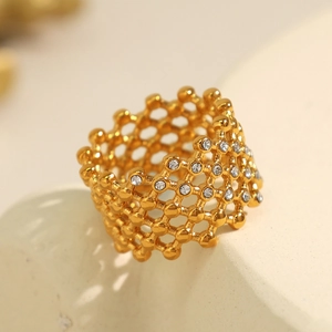 Gold honeycomb hollow ring with crystal stones on a textured neutral background