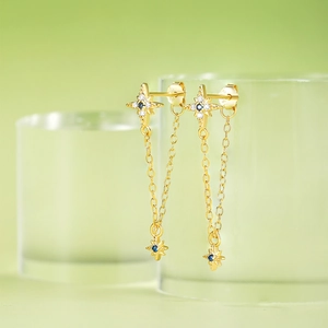 Detail of gold star tassel earrings with blue zircon hanging on a glass rim