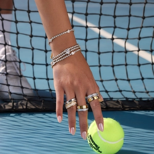Close-up of 18K gold stainless steel tennis bracelets and rings on a tennis court