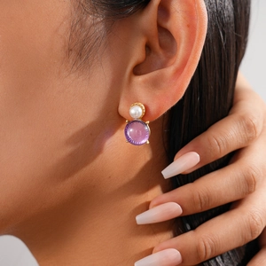 Close-up of golden drop earrings featuring white pearls and faceted purple gemstones
