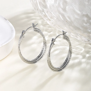 Macro shot of silver triple-layered textured hoop earrings on a reflective surface
