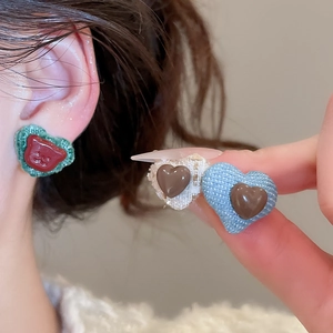 Detailed macro view of heart-shaped fabric stud earrings with denim texture and bear charms