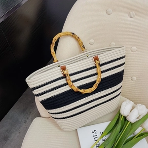 Fashion woven tote bag with black and white stripes and natural bamboo handles on sofa