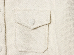 Detail of cream white tweed jacket showing the flap pocket and fabric-covered button
