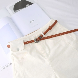 Detail of vintage carved silver buckle on a slim brown leather belt over white trousers