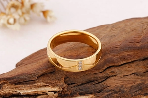 Détail d'une bague en acier titane doré avec zircons sur un support en bois texturé