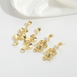 Golden abstract wavy and leaf-shaped metal earrings set on white silk background