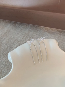 Detailed view of silver bow-shaped ear cuffs with long bead chain tassels on a ceramic plate
