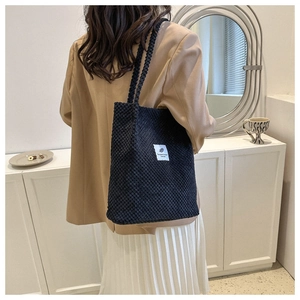 Model wearing a black corduroy bucket bag with long straps over a khaki blazer