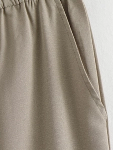 Detail of oatmeal linen pants showing elastic waistband, side pockets and woven texture
