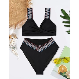 Flat lay of high-waisted black bikini with colorful geometric embroidery and beach accessories