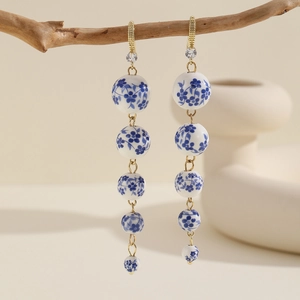 Detail of long blue and white porcelain bead drop earrings hanging on a natural branch