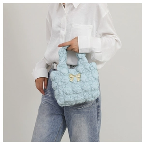 Detail of light blue quilted handbag featuring a golden metal bow and puffed heart texture