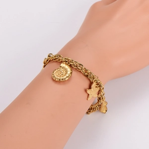Gold stainless steel chain bracelet with sea shell and starfish charms on a model's wrist