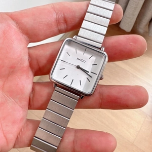 Close-up of a square silver quartz watch with white dial and elastic stainless steel band