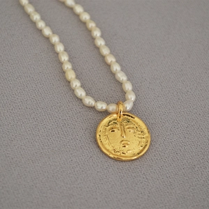 Detailed close-up of a vintage coin pendant on a freshwater pearl necklace on grey fabric