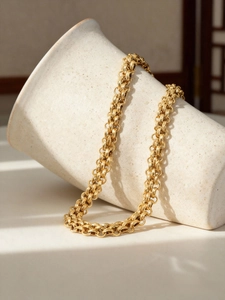 Detail of 18k gold plated chunky chain necklace draped over a textured ceramic vase