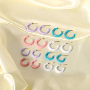 Colorful C-shaped stainless steel earrings in pastel enamel on glossy silk background