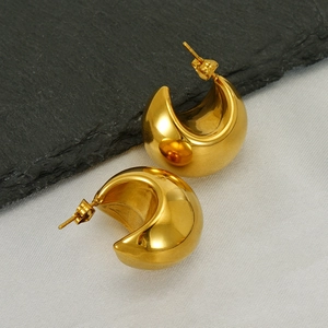 Macro shot of mirror-polished gold-plated crescent dome earrings on stone surface