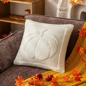 Detail of white plush pumpkin pillowcase with maple leaves on a cozy brown sofa