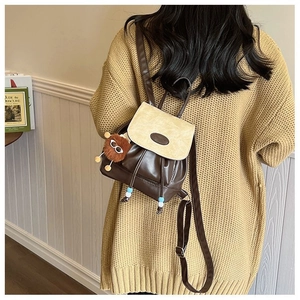 Brown patchwork mini backpack with plush charm worn on a beige knit sweater
