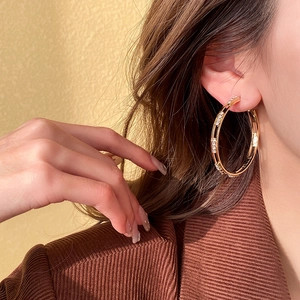 Detail of gold geometric hoop earrings with crystals worn by a model in close-up view