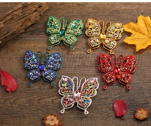 Détail de cinq broches papillons colorées avec strass sur une surface en bois naturel