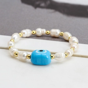 Macro detail of freshwater pearl bracelet with blue evil eye charm on book background