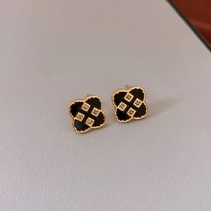 Detailed close-up of gold-plated four-leaf clover earrings with black inlay and small diamonds