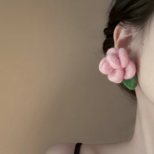 Detail of pink flocked flower earring with green leaf on model's ear in soft light