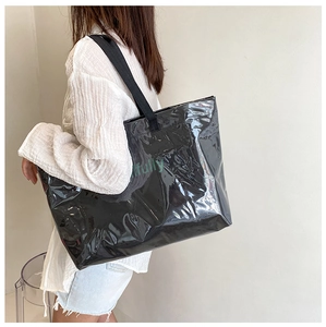 Model wearing a large black glossy jelly tote bag with green fully text on the back