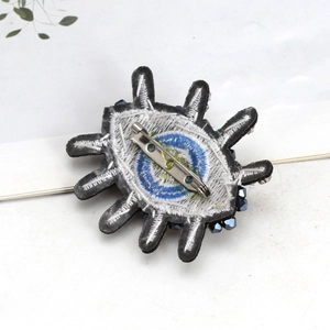 Close-up of the back side of an embroidered evil eye brooch with a metal safety pin