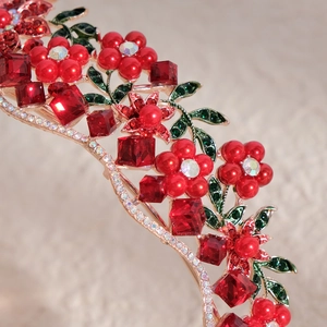 Elegant gold bridal crown featuring red pearls, gemstones, and green enamel leaves