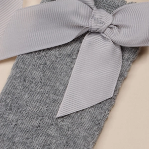 Détail de la chaussette de bébé en maille grise avec un nœud en satin et texture aérée