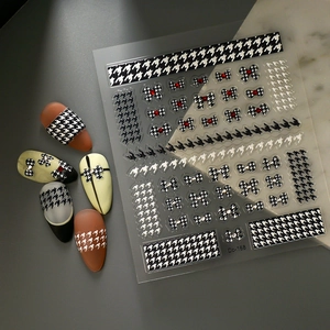 Detail von Hahnentritt-Nagelaufklebern mit 3D-Schleifen und Strass auf grauem Marmor