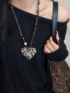 Dettaglio del ciondolo a cuore in peluche leopardato con perla su un maglione nero