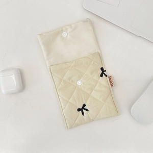 Close-up of beige quilted makeup bag with black bow tie and snap button closure
