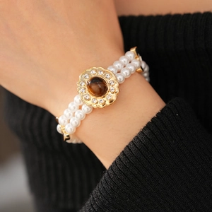 Dettaglio del bracciale di perle multifilo con chiusura a fiore dorato e pietra marrone