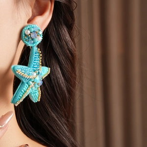 Detail of a handmade turquoise beaded starfish earring with pearls on a model