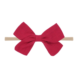 Detail of red fabric bow on skin-tone nylon headband for infants with studio lighting