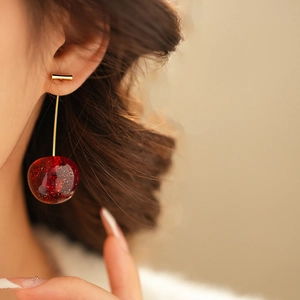 Close-up of cherry resin earrings with red translucent glitter balls and gold metal bars