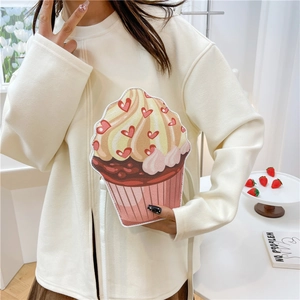 Cute cupcake-shaped crossbody bag with red heart pattern held by a girl in cream sweater