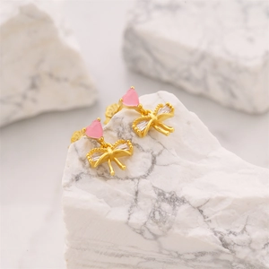 Macro detail of golden bow earrings with pink heart-shaped stone and white zircon