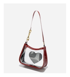 Close-up of red patent leather and PVC transparent crossbody bag with heart logo and gold chain