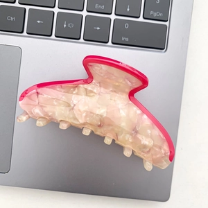 Detail of a marble pattern hair claw clip with vibrant rose red edges on a laptop surface