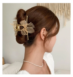 Détail d'une grande pince à cheveux dorée avec un élégant nœud en organza sur un chignon