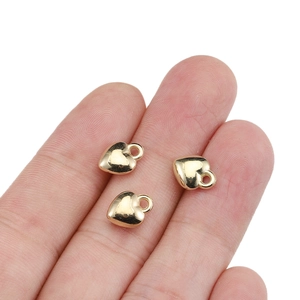 Three tiny gold heart-shaped pendants for jewelry making shown on a fingertip
