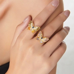 Elegant gold butterfly rings with colorful crystal inlay on model hands in soft light